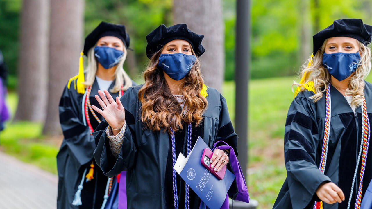 A graduate waves as she walks into the Commencement ceremony