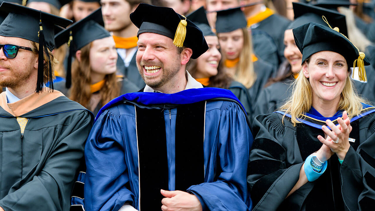 Faculty and graduates laugh in their seats