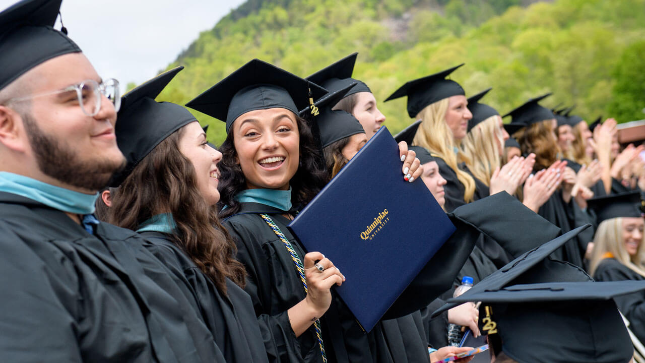 Graduating graduate student holds up their diploma and smiles