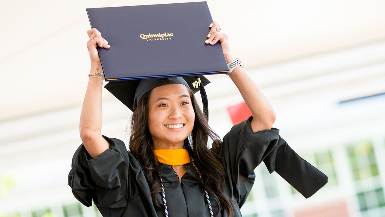 Graduate smiles and holds up diploma over their head on stage