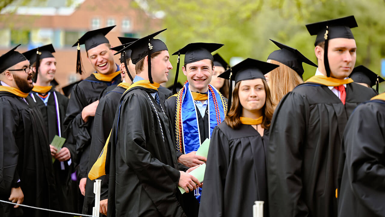 Graduates laugh and converse as they wait to sit down