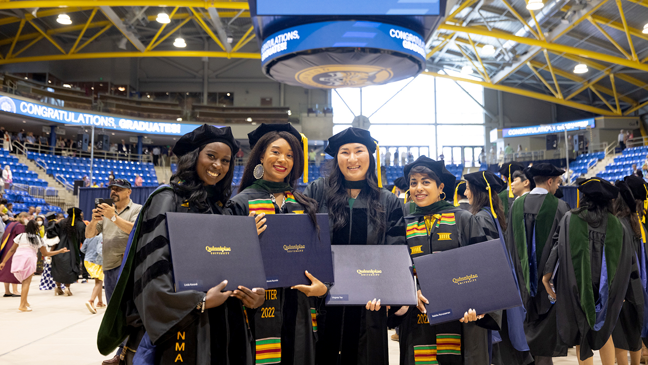 Graduates smile and hold up their diplomas under the People's United Center jumbotron