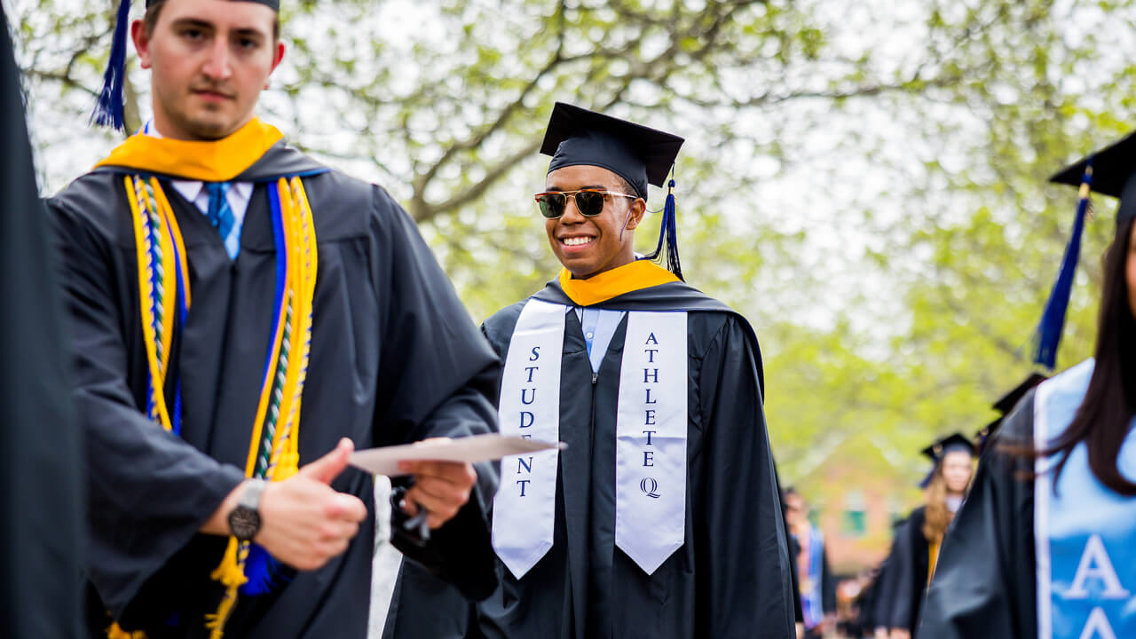 A graduating student athlete smiles on the Quad