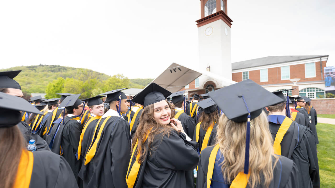 A graduate turns and smiles from a row of graduates as she participates in Commencement