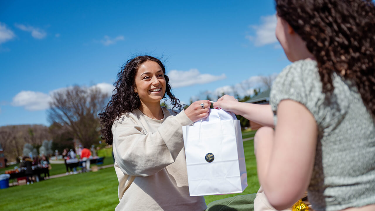 A student hands a bag to another student.