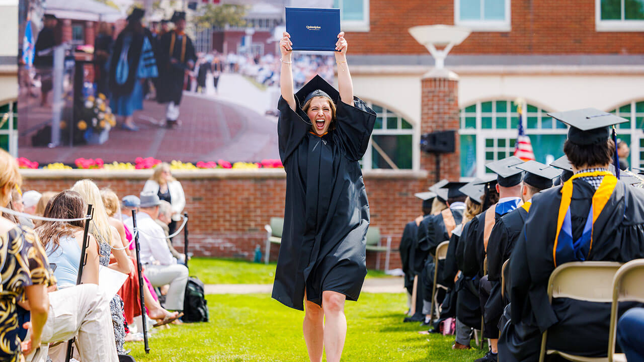 Student holds up her diploma in her cap and gown