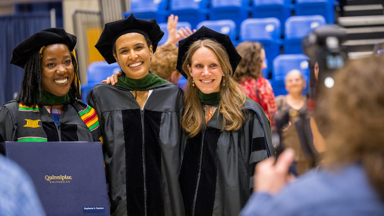 Three graduates stand arm in arm and smile for a photo