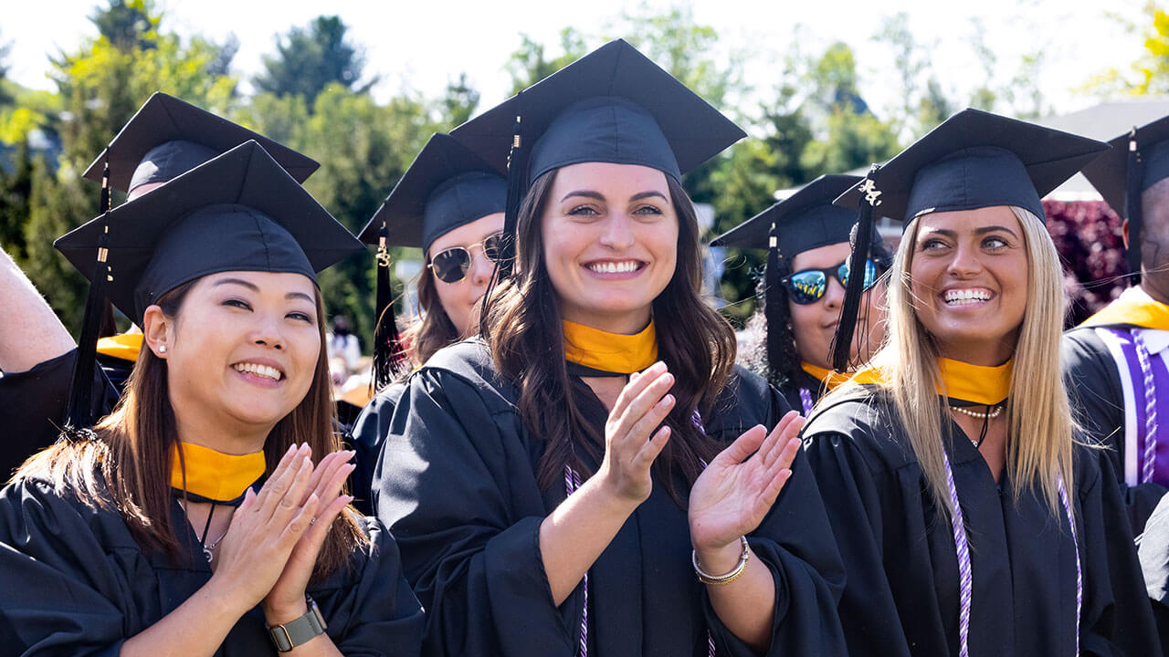 trio of graduates smile and clap in their row