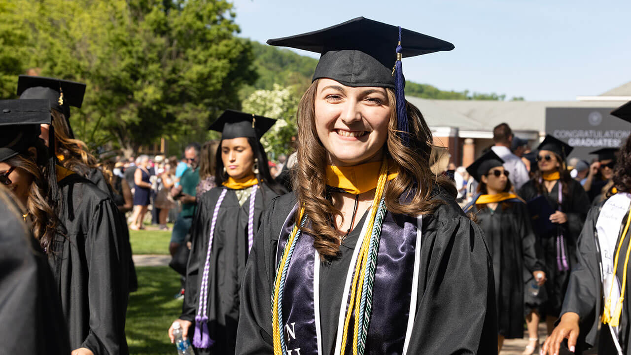 female graduate in a group of graduates smiles directly at the camera