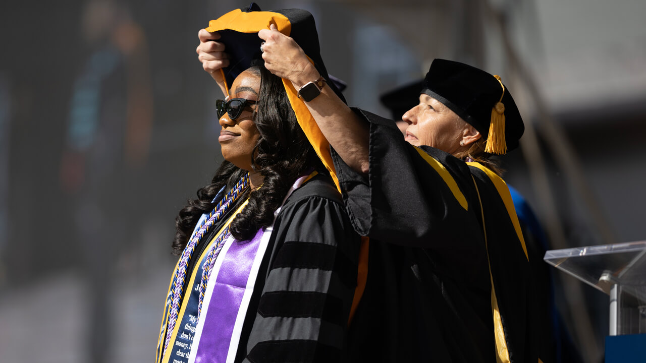 A faculty member lifts a doctoral hood over the head of a graduate