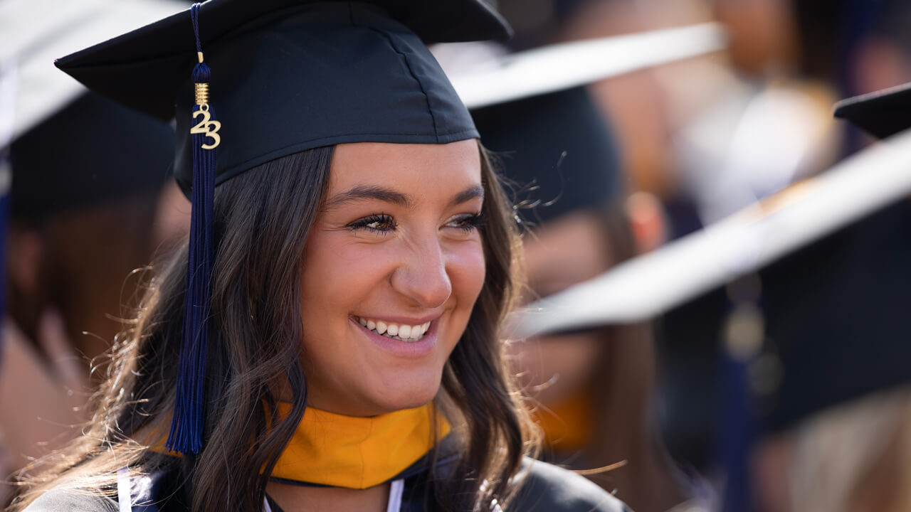 A graduate wears her cap with class of 2023 tassel and smiles