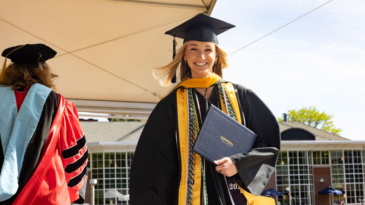 Graduate holds diploma to her chest while grinning happily