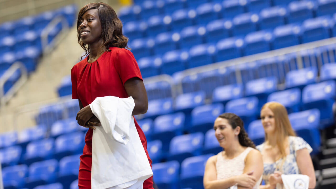 Student standing wearing a red dress and holding her white coat