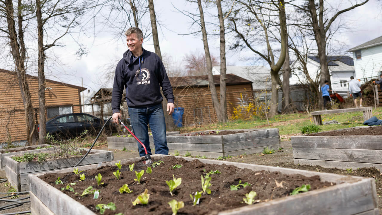 A professor stands near a garden