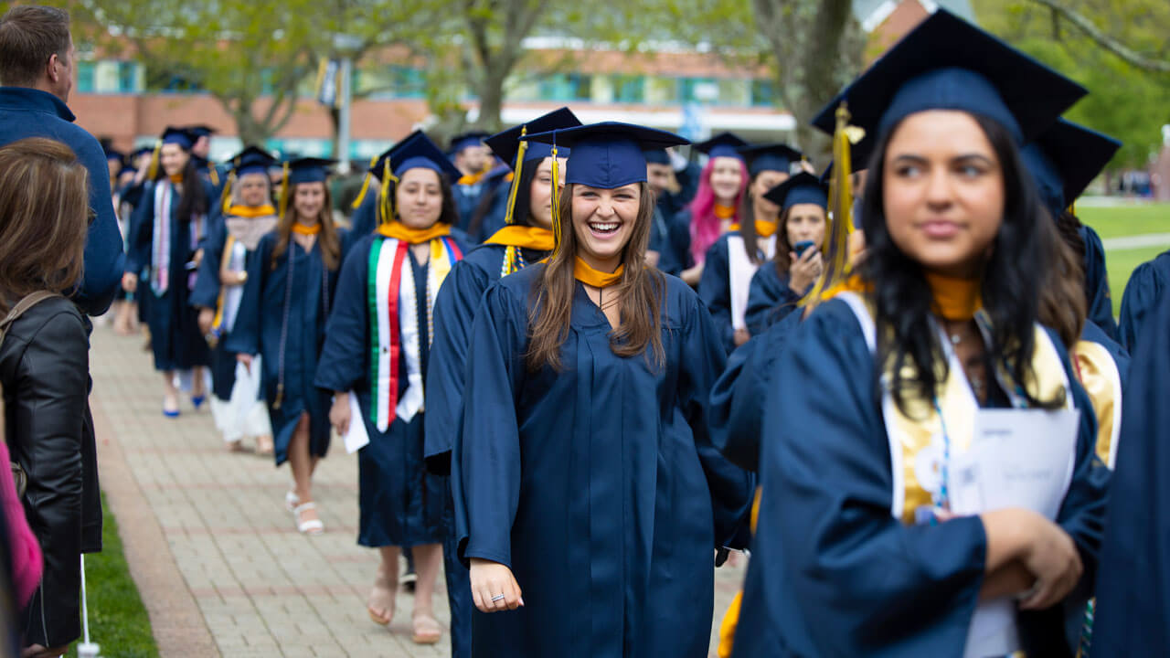 A line of graduates processes down the brick walkway across the quad