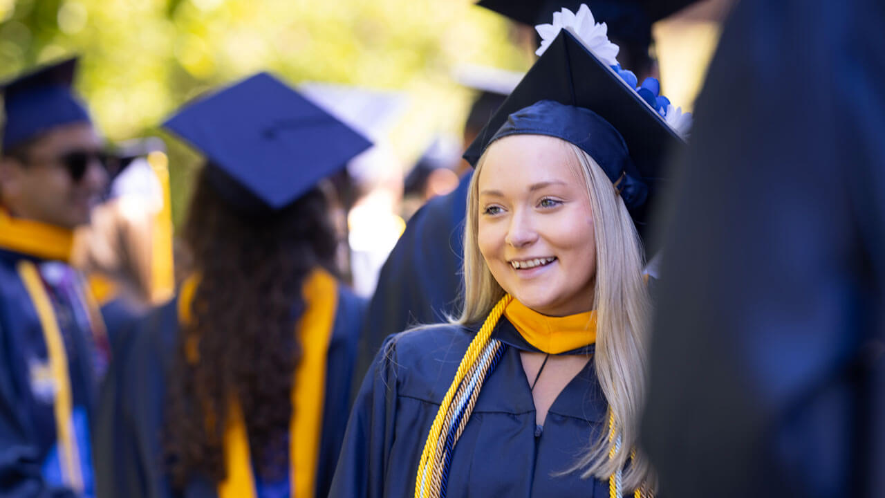 2024 School of Business graduate student grins with pride in their cap and gown.