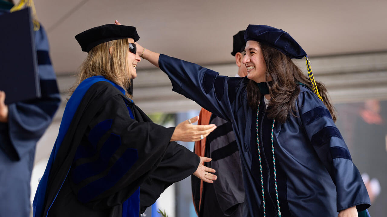 Ecstatically, a class of 2024 graduate student reaches to hug one of their administrators on stage.