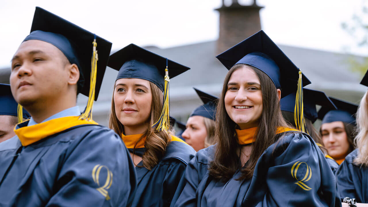 A 2024 health science graduate smiles brightly at the camera from their seat.