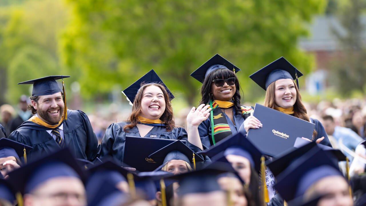 Four graduates stand, smile and cheer