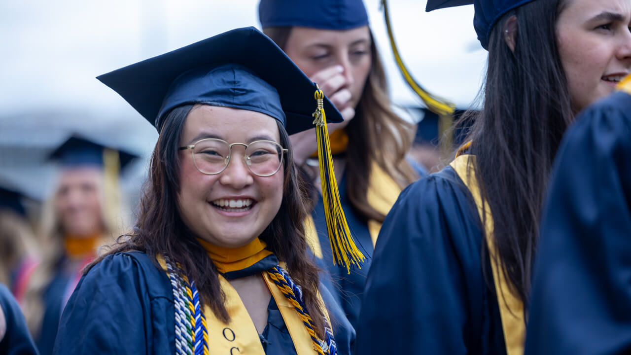 A graduate with a gold stole and several honor cords smiles broadly