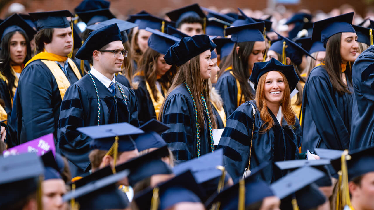 Dozens of graduates clap and cheer from their seats during health sciences Commencement