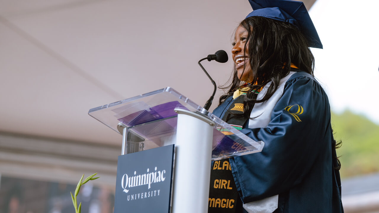 A graduate speaks from the podium with a microphone from the library steps