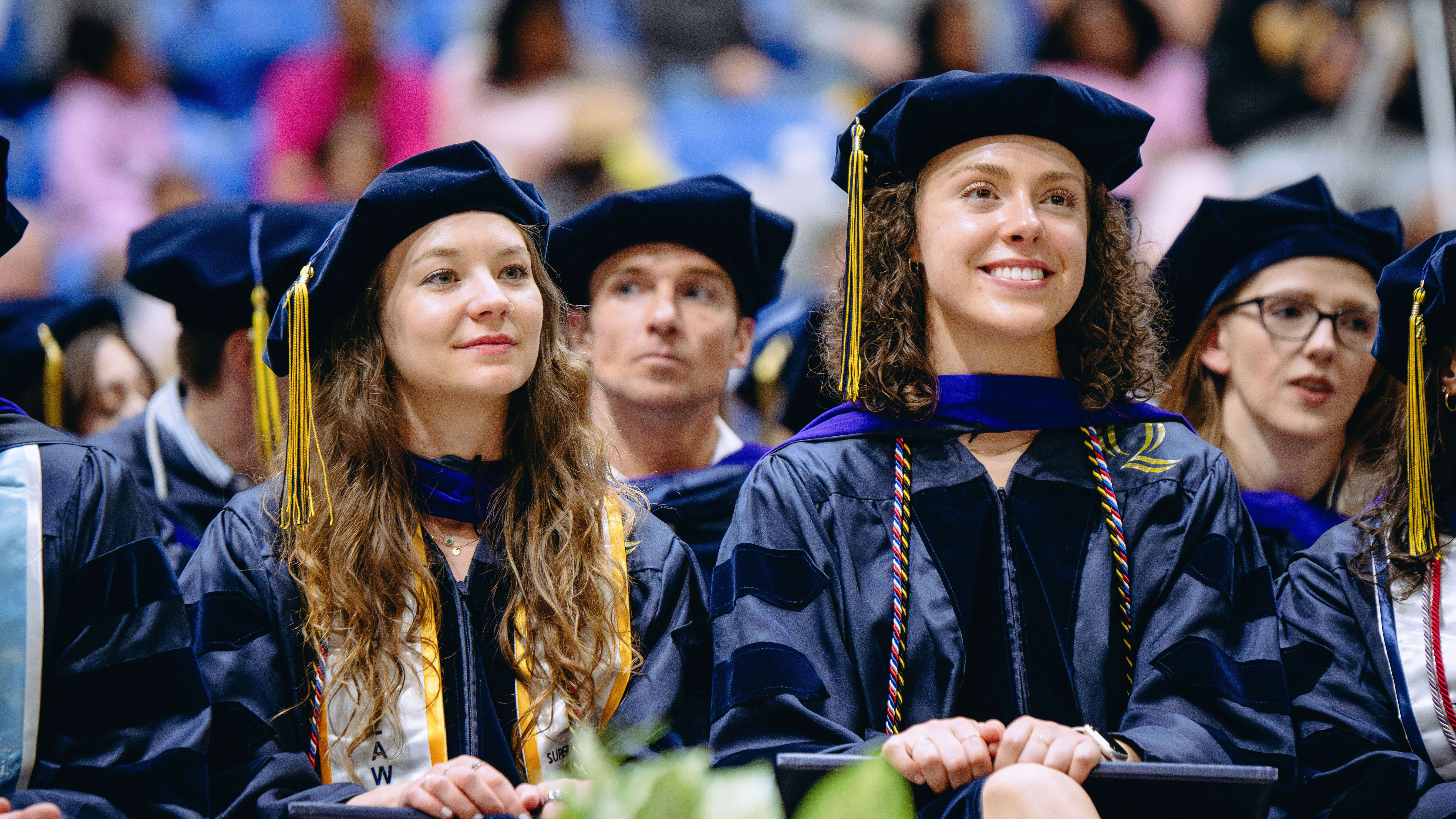 Class of 2024 School of Law Graduate smile as they sit watching the stage