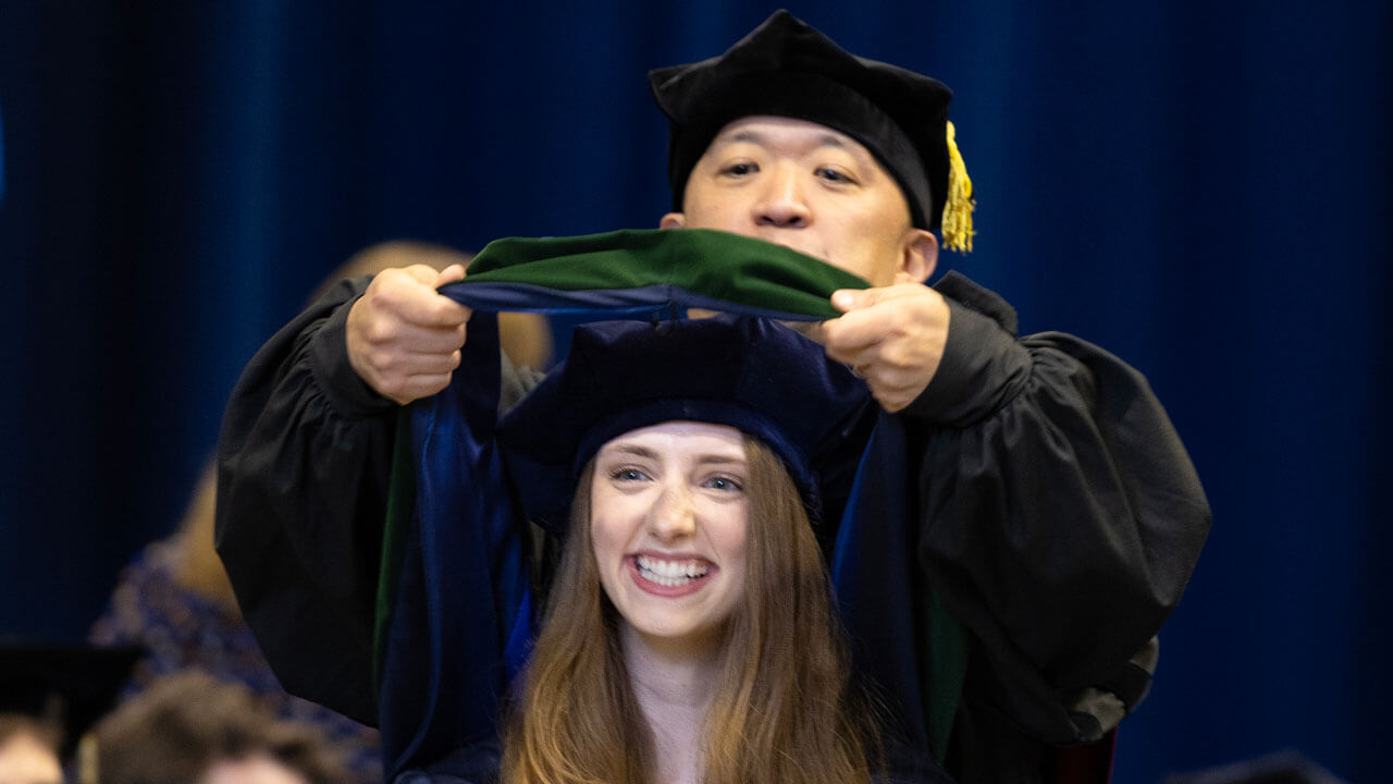 Family member hoods medicine graduate, smiling at the crowd