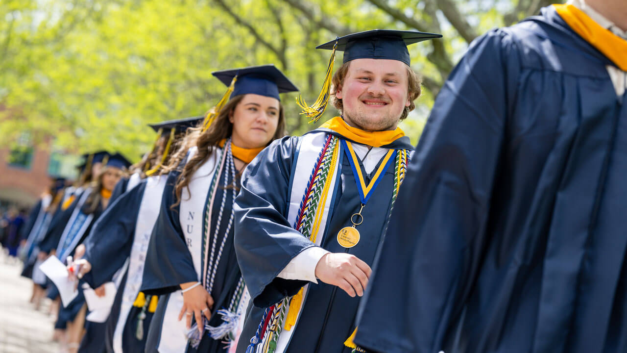 A School of Nursing graduate smiles happily while walking across the quad to take their seat.