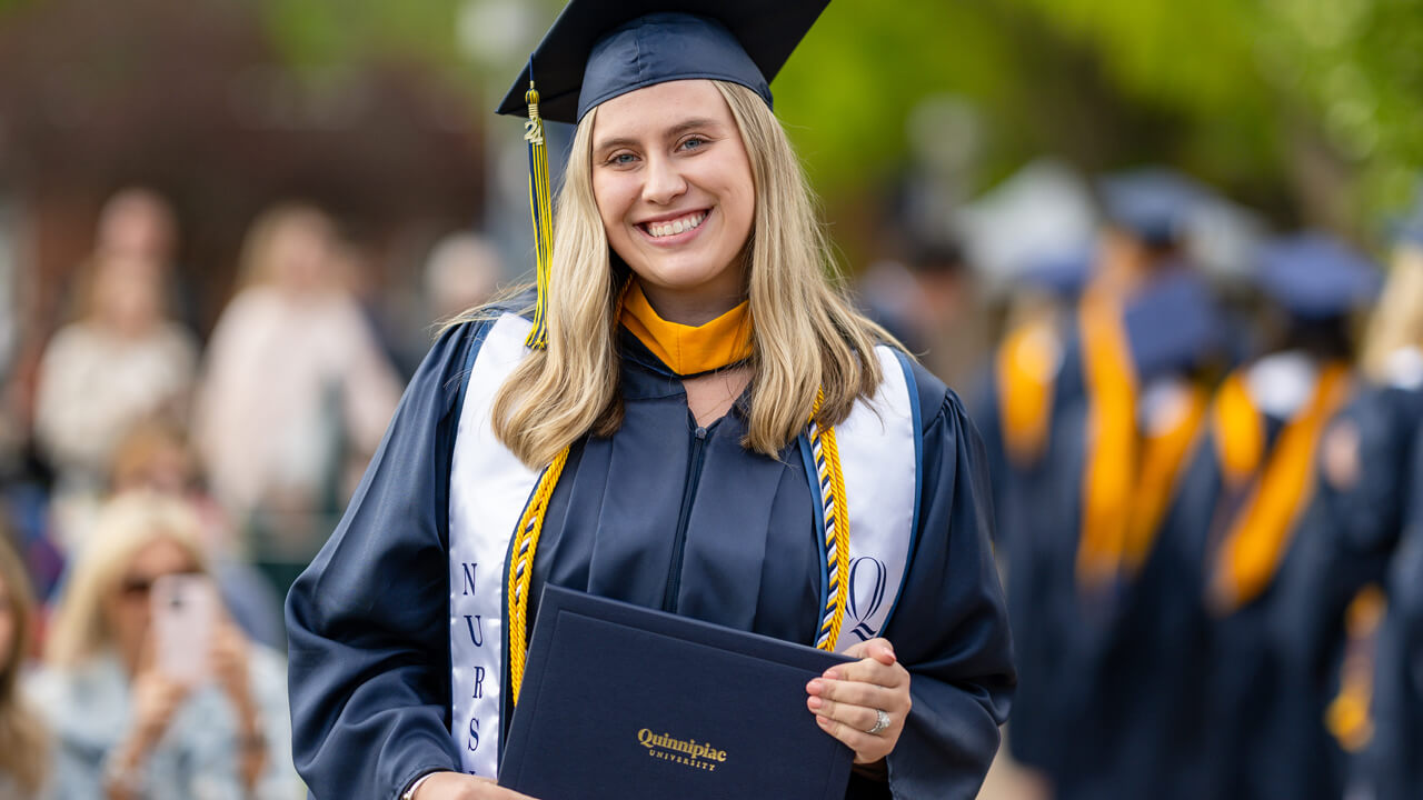 A graduate in a white stole pauses and smiles for a photo