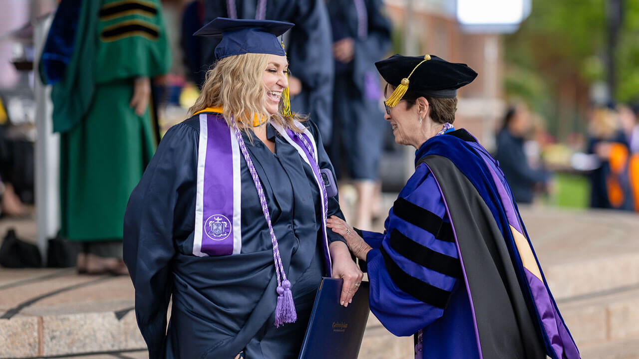 graduate and professor laugh together by the graduation stage