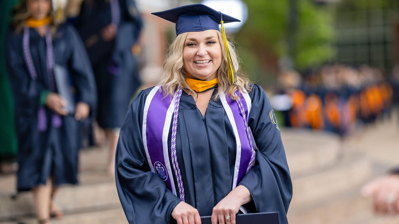 graduate poses with diploma by the stage