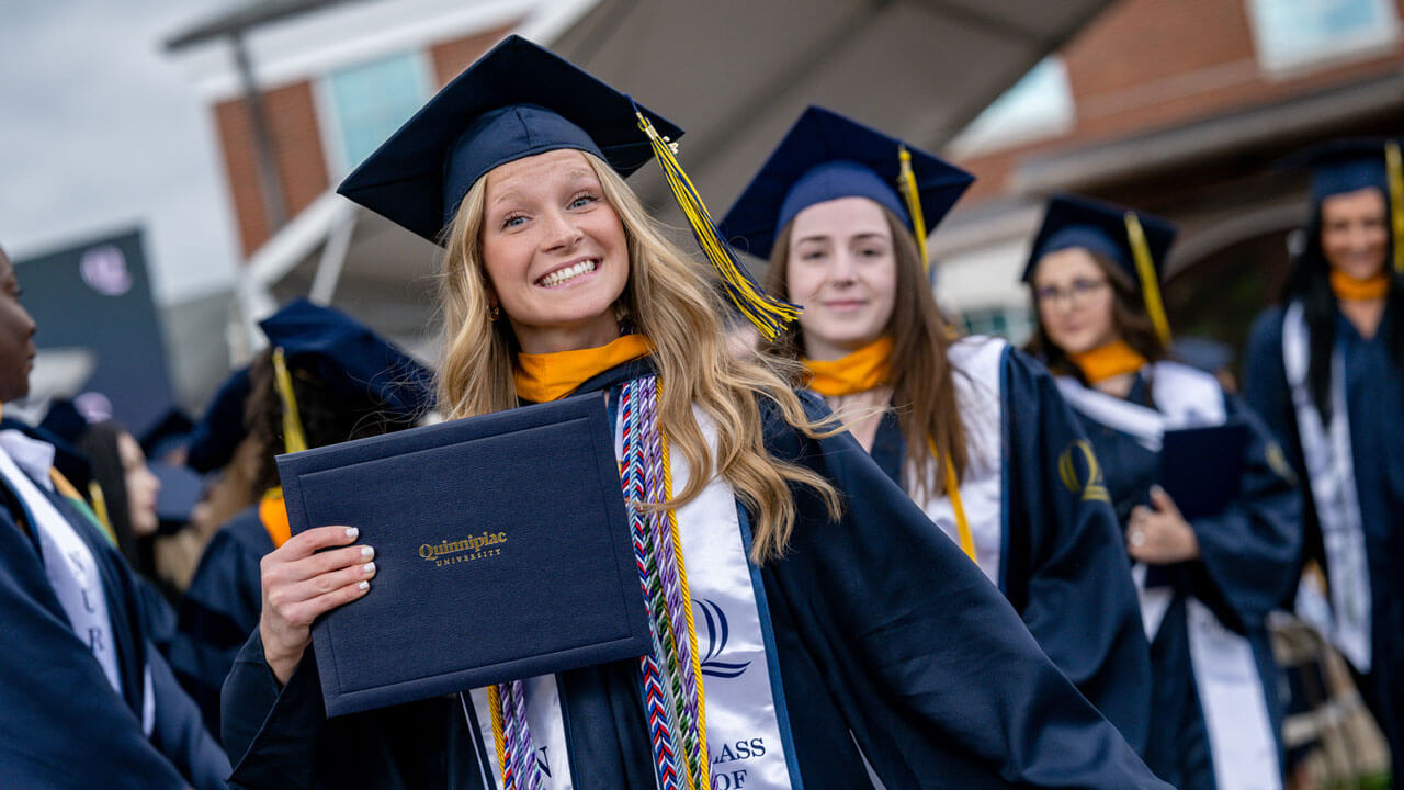 Graduate excitedly holds up their diploma as they walk back to their seat.