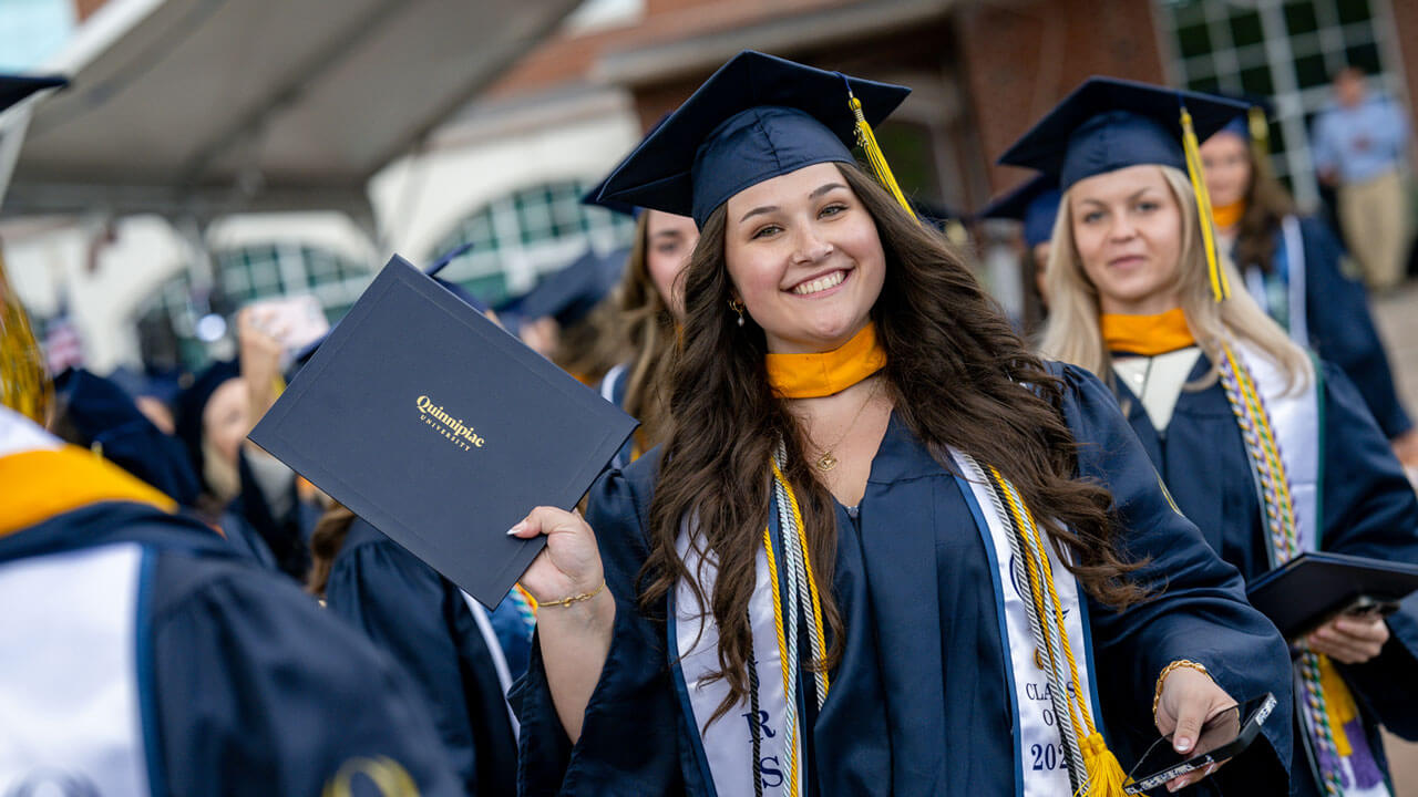 School of Nursing class of 2024 graduate holds their diploma up in the air proudly.