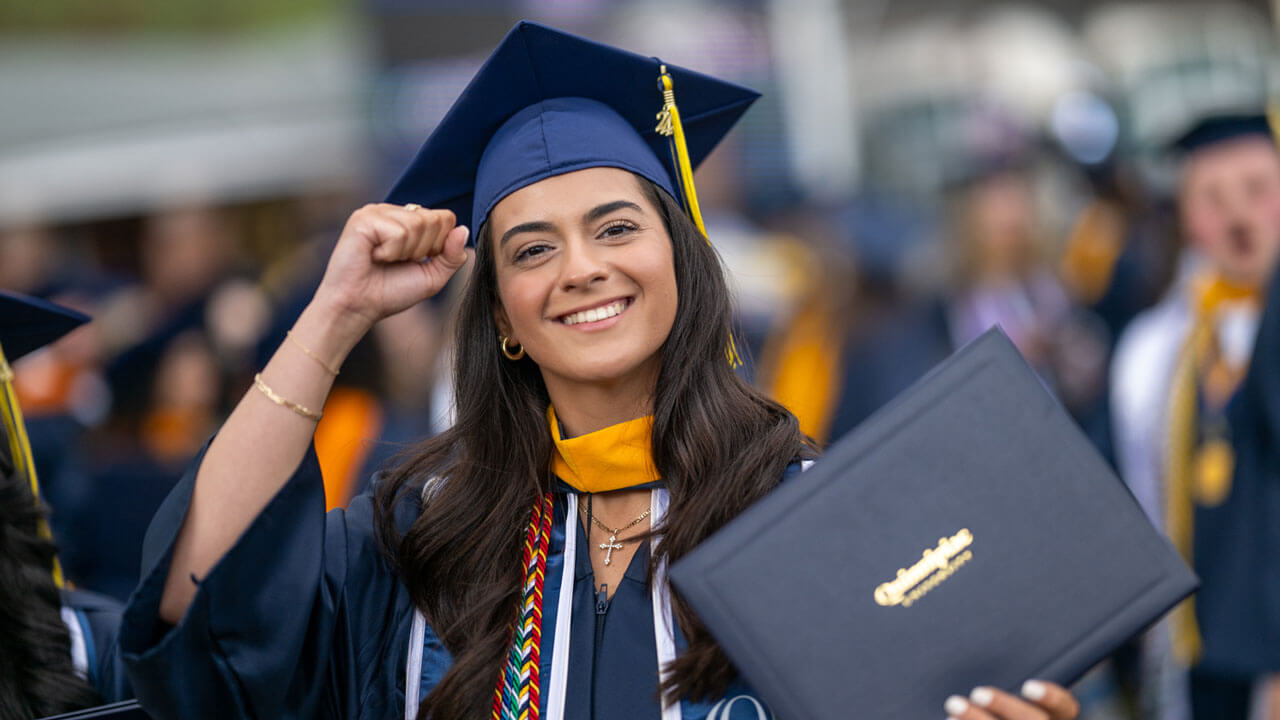 An excited 2024 graduate raises their fist in the air in celebration after receiving their diploma.