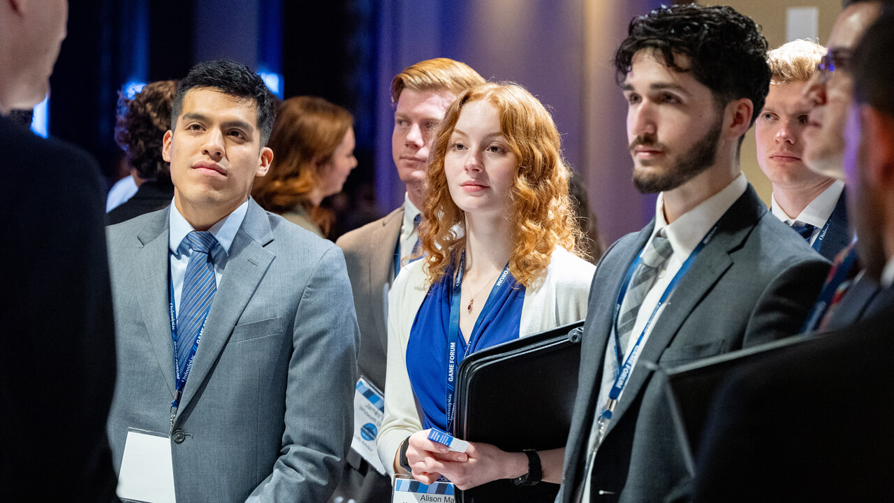 Half a dozen business students in suits speak with a professional