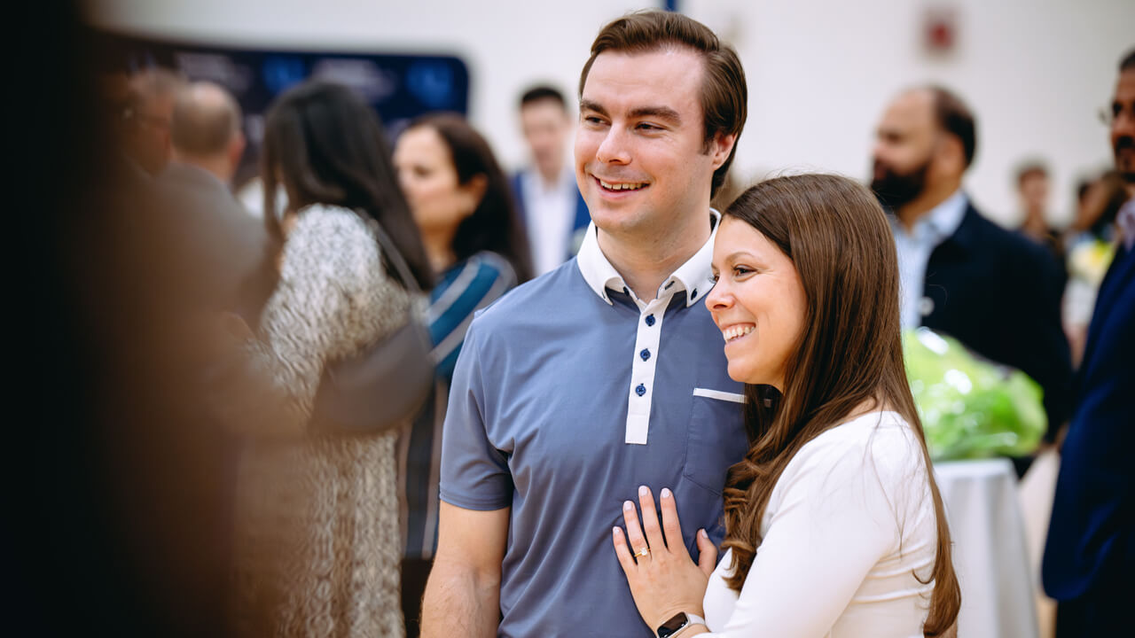 Two people embrace and smile as a family member takes their photo