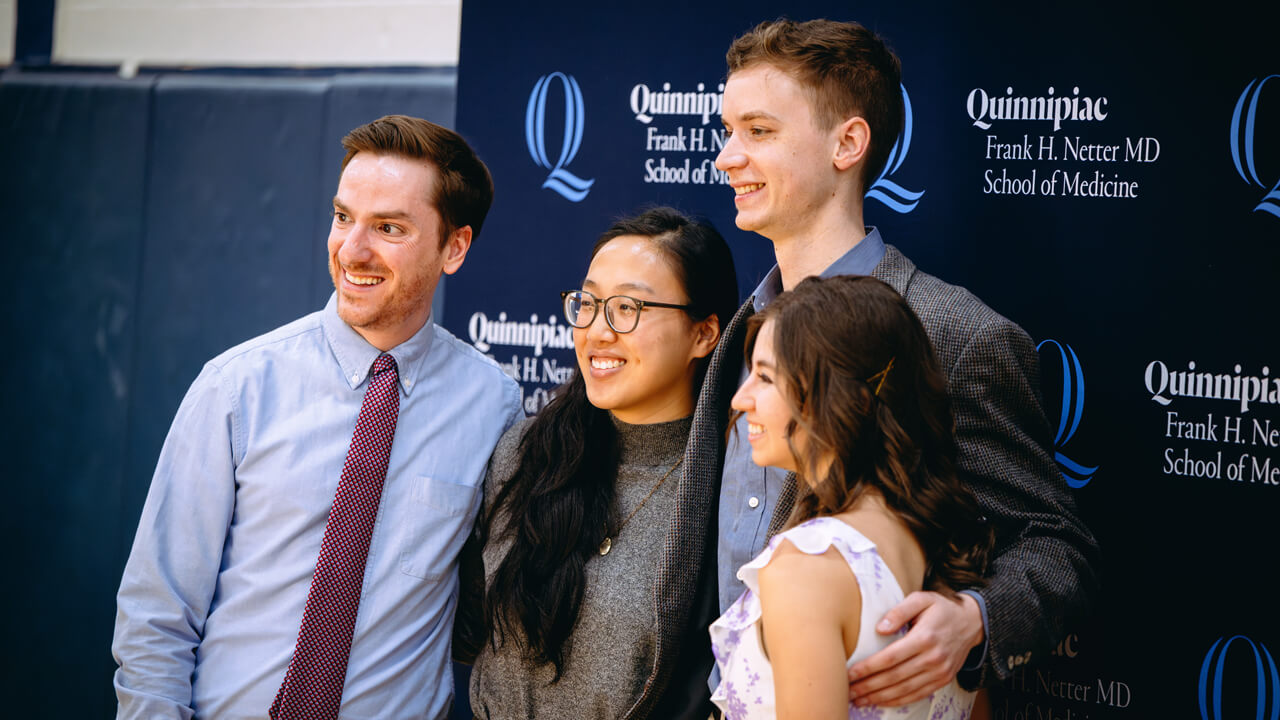 Four people pose for a photo in front of the Frank H. Netter MD School of Medicine backdrop