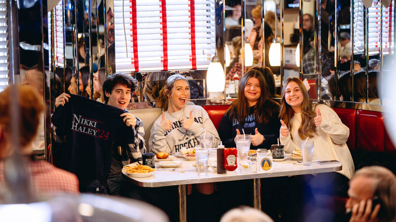 Quinnipiac students sitting in New Hampshire diner booth holding a Nikki Haley '24 shirt