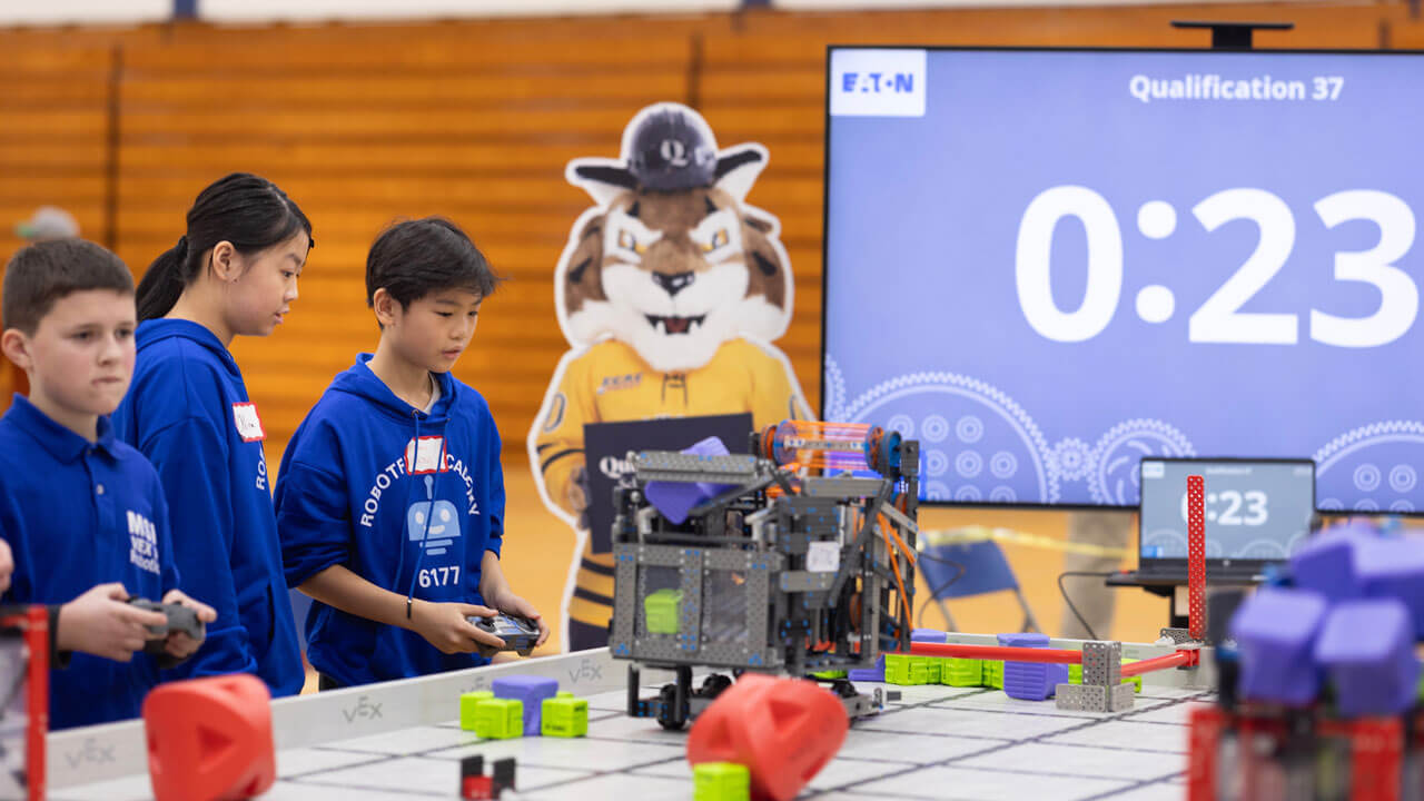 Boomer the Bobcat poster behind students operating robots