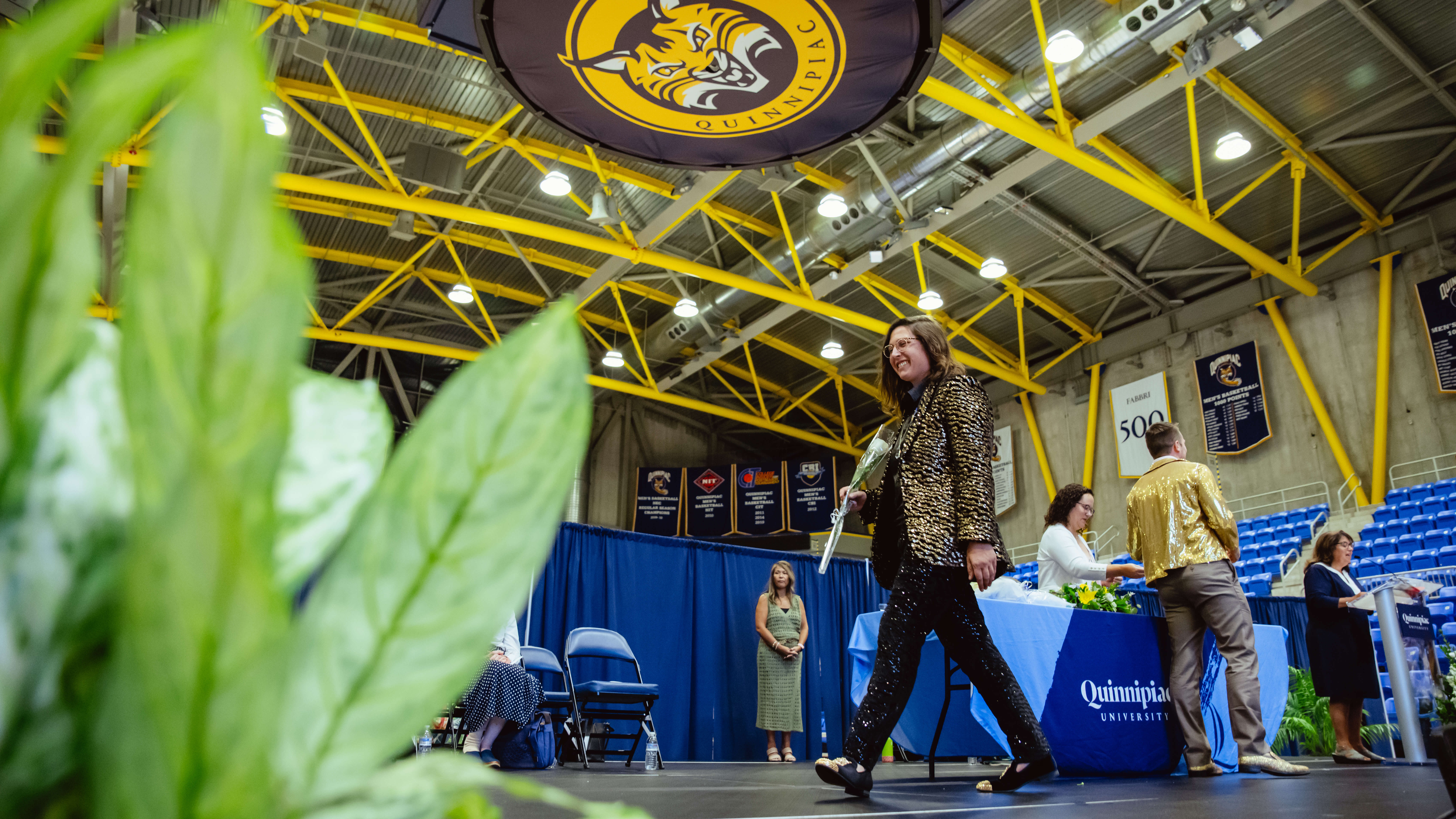 A graduate walks across the stage with her rose and pin