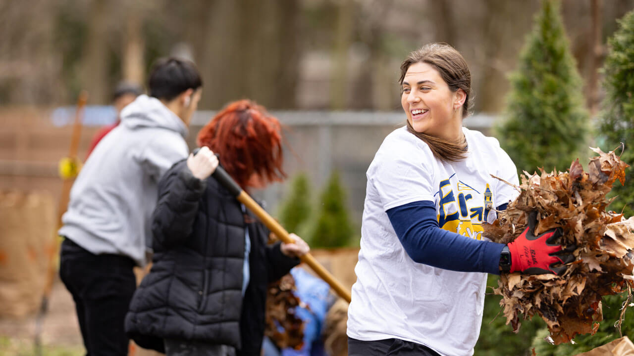 Student smiles while carrying a pile of leaves