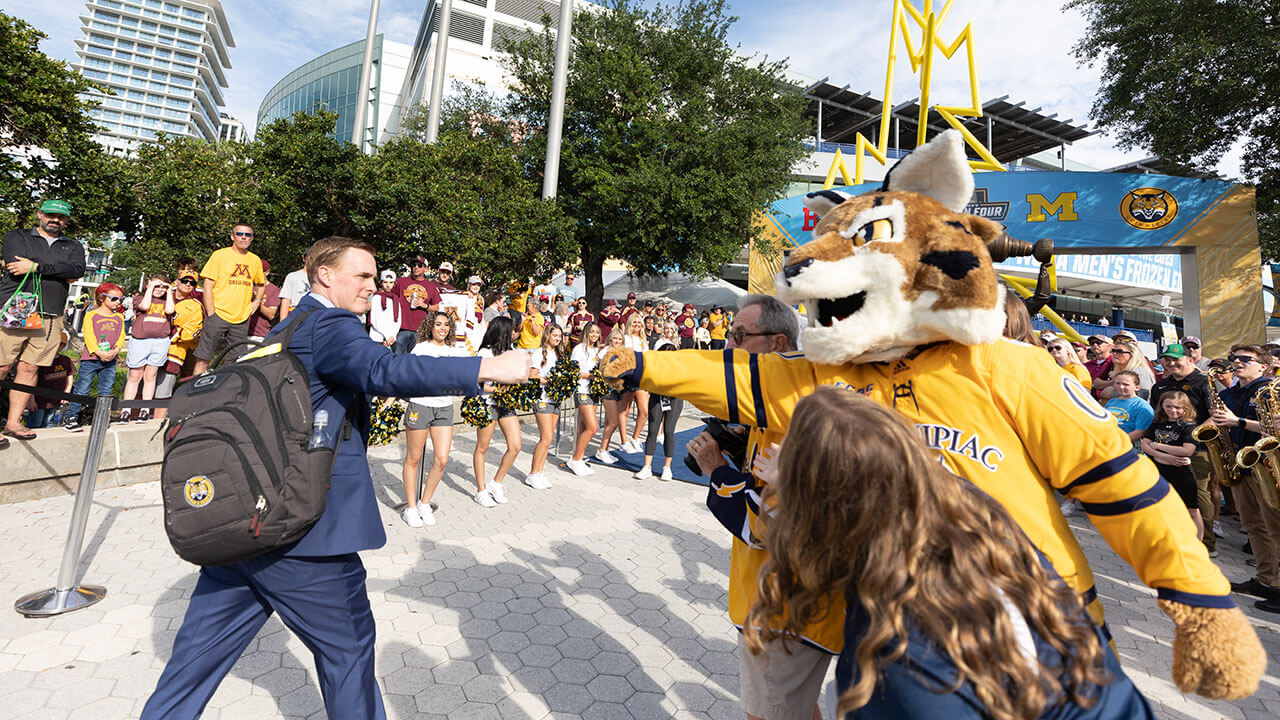 Boomer the bobcat mascot fist bumps men's ice hockey coach Rand Pecknold as he walks down the blue carpet