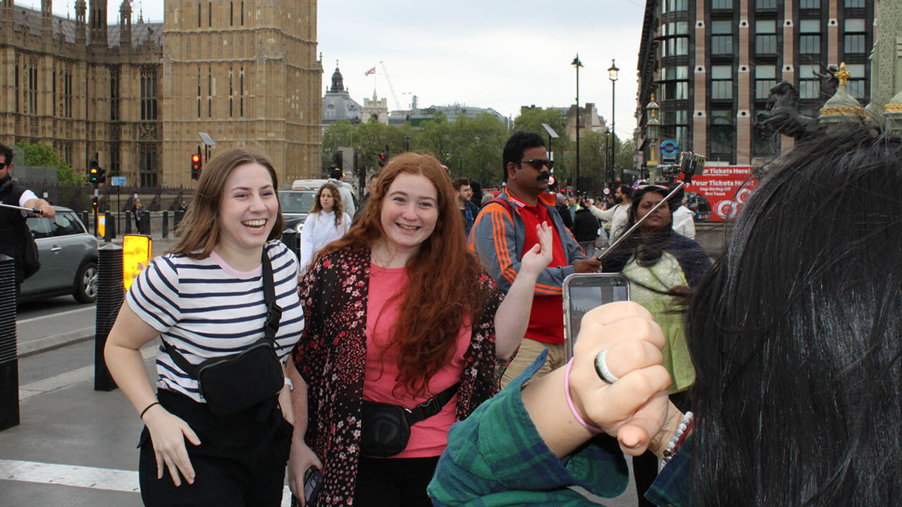 two students smile as a third points at them behind a phone