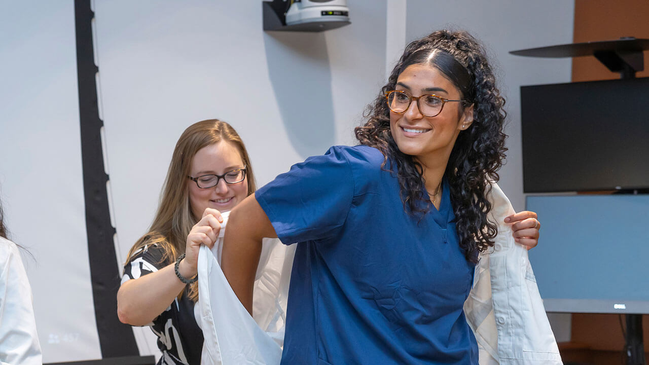 nursing student has her white coat put on her by her advisor