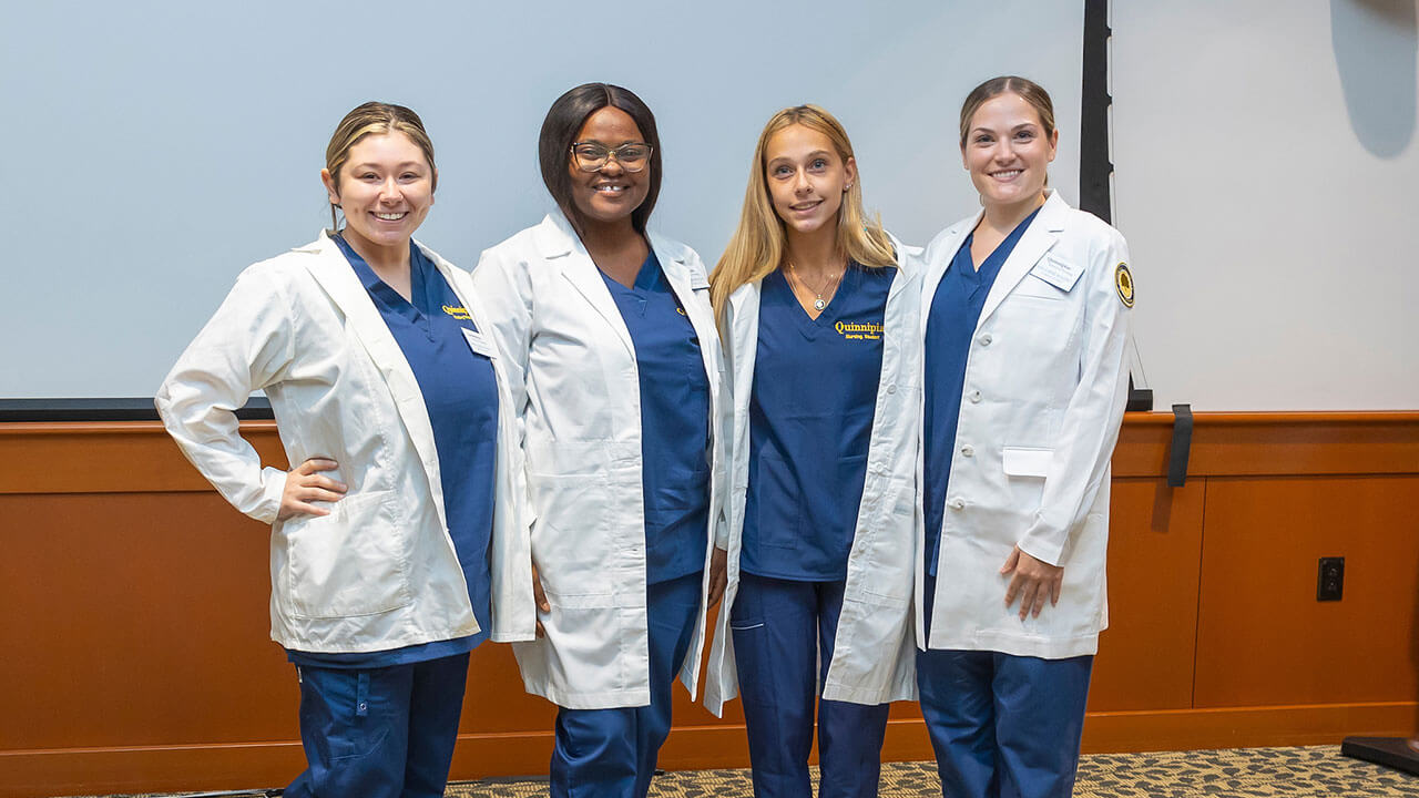 four nursing students in white coats pose for a photo