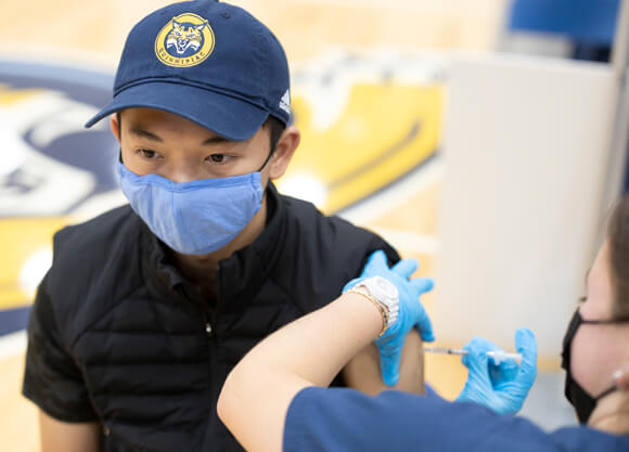 A student sits and receives a flu vaccine from a healthcare provider