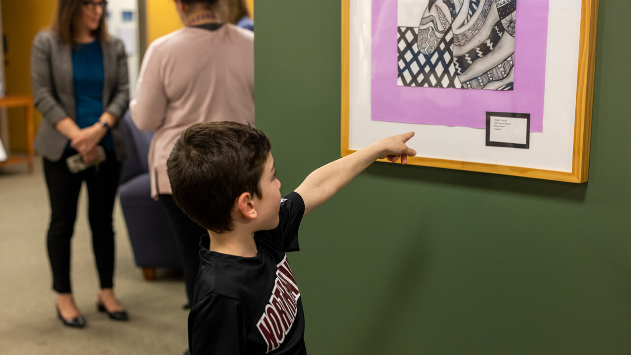 a young boy pointing to a piece of art on a wall