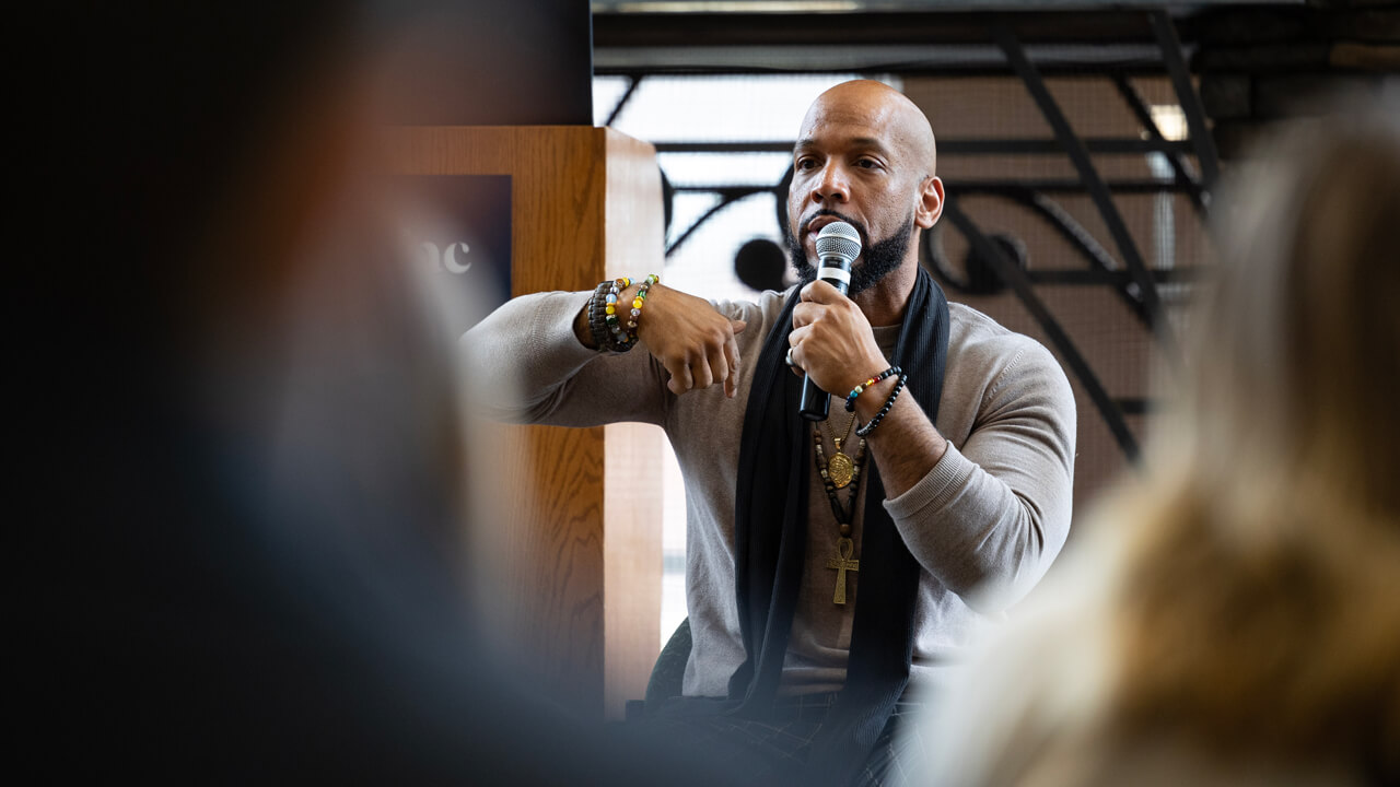 A presenter speaks into a microphone in front of people seated in the Piazza in the student center