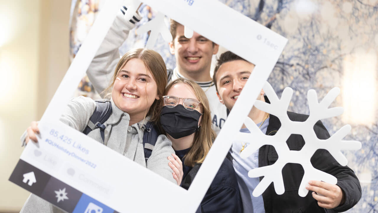 Group of friends holding up QU Dining Instagram prop and smiling for photo